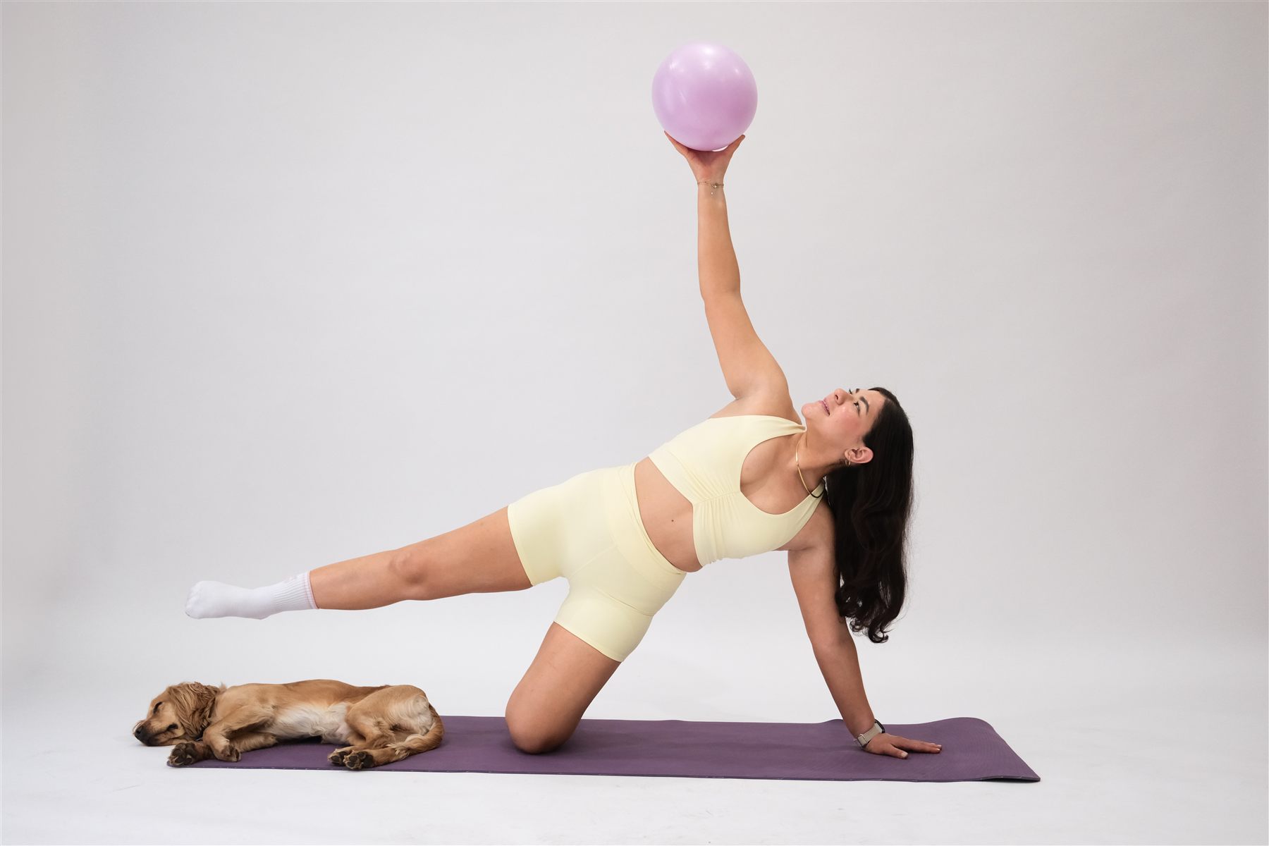 Valeria Blanco in a side plank holding a Pilates ball overhead